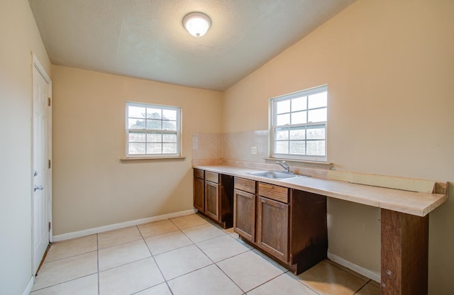 kitchen featuring plenty of natural light, light tile patterned flooring, sink, and vaulted ceiling