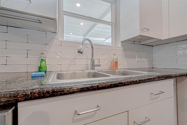 room details featuring backsplash, sink, white cabinets, and dark stone counters