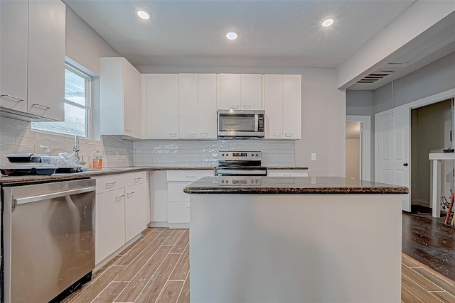 kitchen featuring a kitchen island, white cabinetry, stainless steel appliances, and dark stone counters