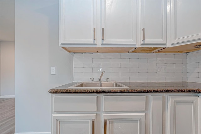 kitchen with backsplash, dark stone countertops, white cabinetry, and sink