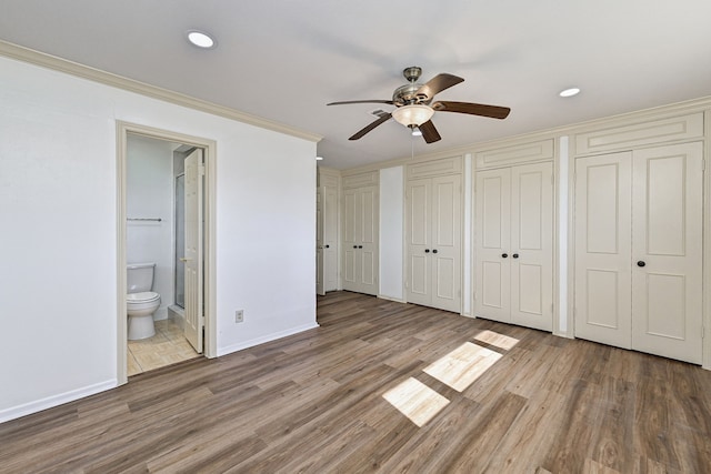 unfurnished bedroom with connected bathroom, two closets, light hardwood / wood-style flooring, and ceiling fan