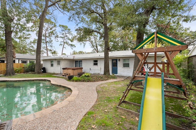 back of house with a playground and a pool with hot tub