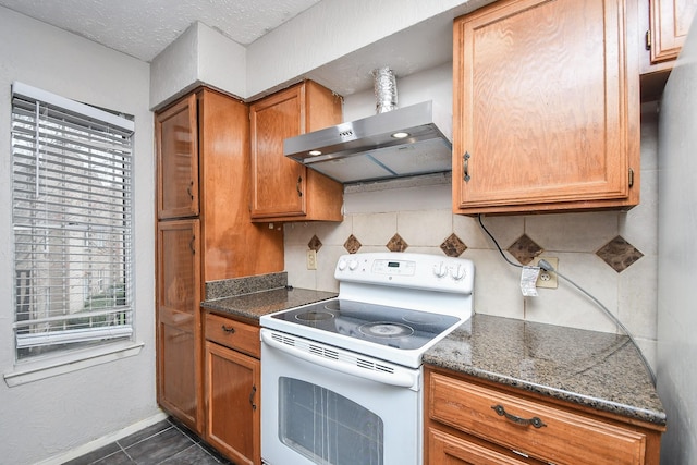 kitchen featuring dark stone counters, dark tile patterned flooring, electric stove, wall chimney range hood, and decorative backsplash