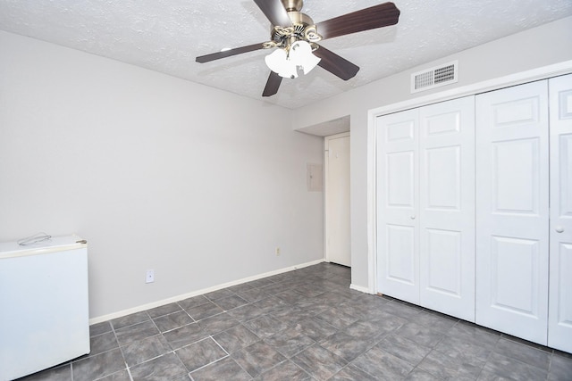 unfurnished bedroom with a textured ceiling, refrigerator, a closet, and ceiling fan