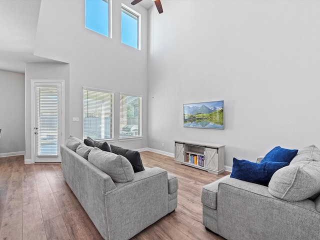 living room featuring ceiling fan, wood-type flooring, plenty of natural light, and a high ceiling