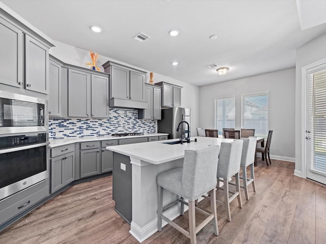 kitchen featuring a breakfast bar area, visible vents, gray cabinetry, appliances with stainless steel finishes, and a sink