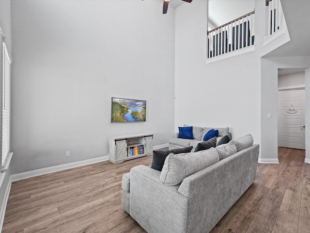 living area featuring a towering ceiling, hardwood / wood-style flooring, baseboards, and a ceiling fan