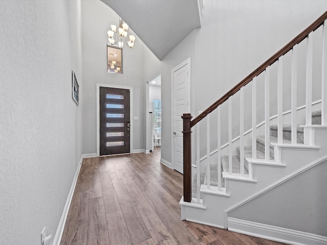 foyer entrance with high vaulted ceiling, stairway, a chandelier, baseboards, and hardwood / wood-style flooring