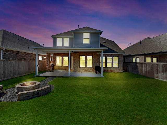 back of property at dusk with a yard, an outdoor fire pit, a fenced backyard, and brick siding