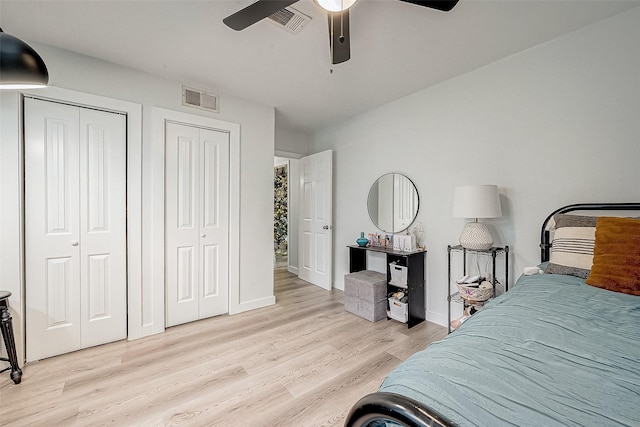 bedroom featuring ceiling fan, two closets, and light hardwood / wood-style floors