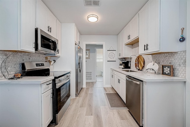 kitchen with decorative backsplash, stainless steel appliances, sink, light hardwood / wood-style flooring, and white cabinets