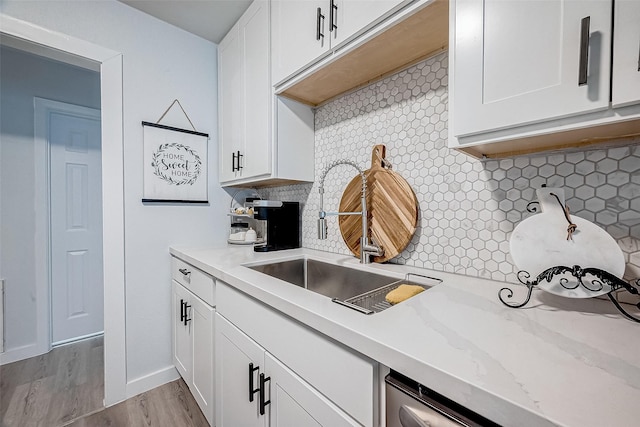 kitchen with sink, light stone counters, light wood-type flooring, white cabinets, and backsplash