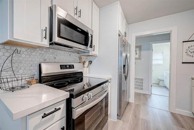 kitchen with appliances with stainless steel finishes, tasteful backsplash, white cabinetry, light hardwood / wood-style floors, and light stone countertops