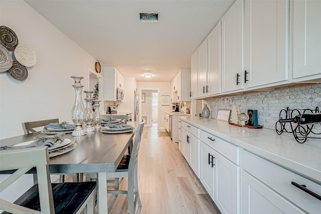 kitchen with backsplash, white cabinetry, stainless steel appliances, and light hardwood / wood-style flooring