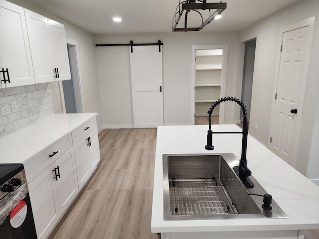 kitchen with sink, a barn door, light hardwood / wood-style flooring, decorative backsplash, and white cabinets