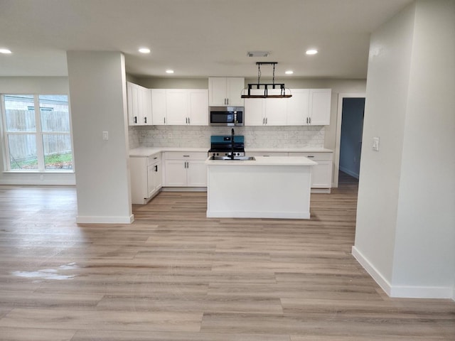 kitchen with light wood-type flooring, sink, pendant lighting, a center island with sink, and white cabinets