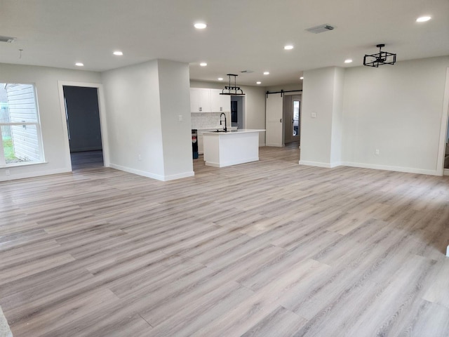 unfurnished living room with a barn door, light hardwood / wood-style flooring, and sink