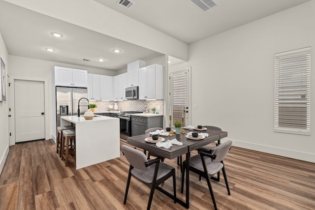 interior space with hardwood / wood-style floors, a center island with sink, appliances with stainless steel finishes, white cabinetry, and a breakfast bar area