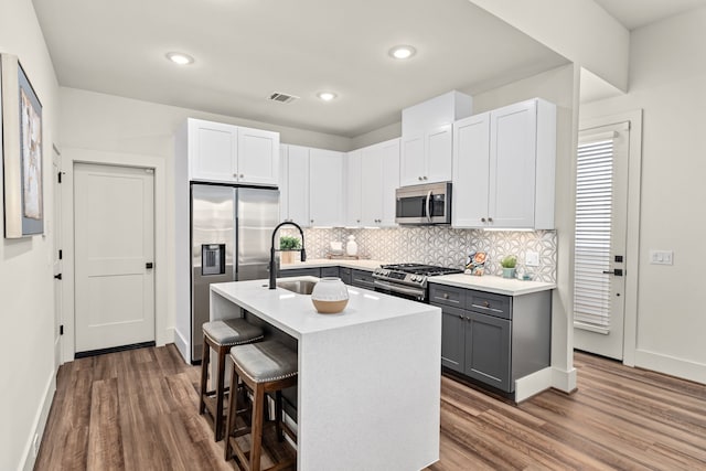 kitchen with gray cabinetry, white cabinetry, an island with sink, a breakfast bar, and appliances with stainless steel finishes