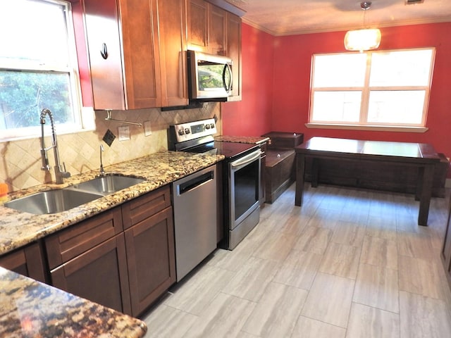 kitchen featuring sink, stainless steel appliances, light stone counters, crown molding, and decorative light fixtures