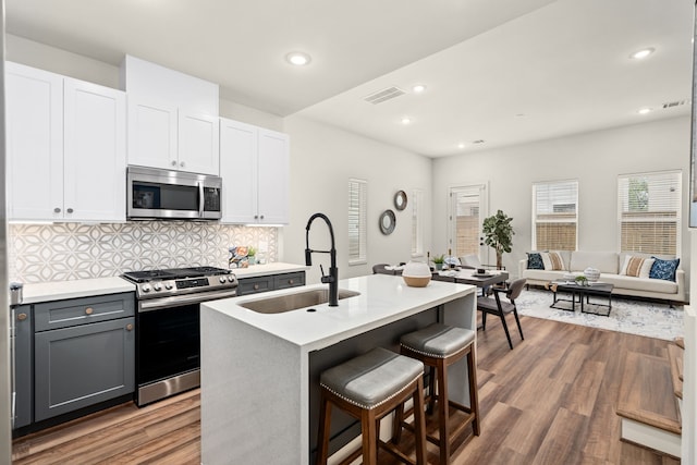 kitchen featuring sink, white cabinetry, stainless steel appliances, a center island with sink, and decorative backsplash