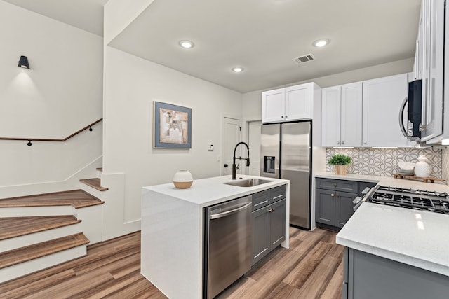 kitchen with sink, gray cabinetry, white cabinets, stainless steel appliances, and a center island with sink