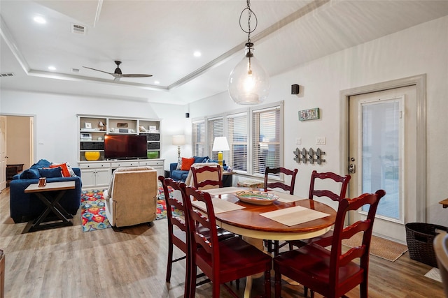 dining space featuring ceiling fan, light hardwood / wood-style floors, and a tray ceiling