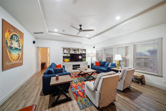 living room with a raised ceiling, ceiling fan, and light wood-type flooring