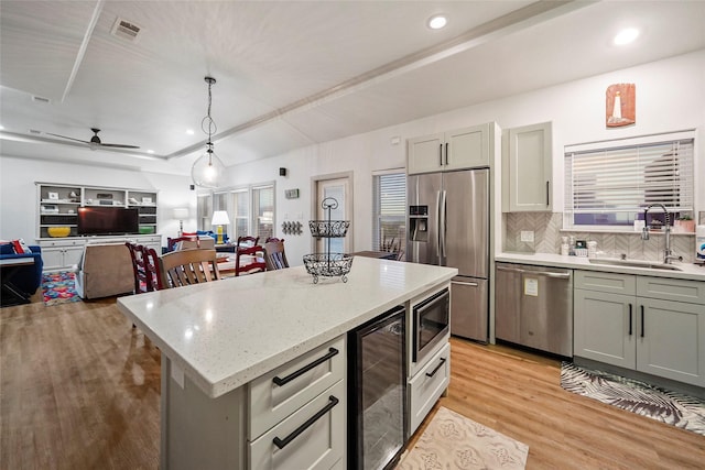 kitchen with appliances with stainless steel finishes, sink, pendant lighting, a center island, and wine cooler