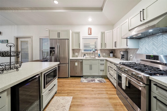 kitchen featuring sink, beverage cooler, stainless steel appliances, light hardwood / wood-style flooring, and backsplash