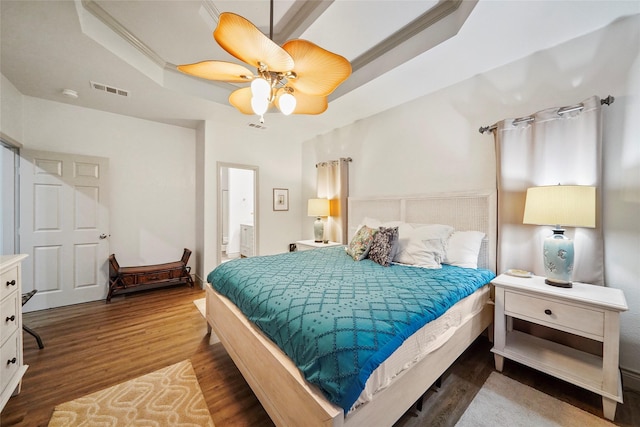 bedroom with ensuite bath, ceiling fan, dark hardwood / wood-style floors, ornamental molding, and a tray ceiling