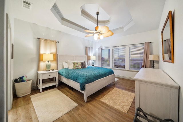 bedroom featuring light hardwood / wood-style flooring, a raised ceiling, ceiling fan, and ornamental molding