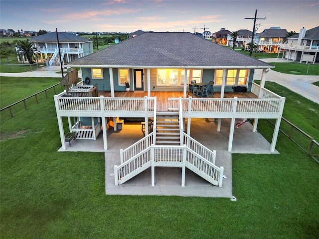 back house at dusk with a deck, a patio area, and a lawn