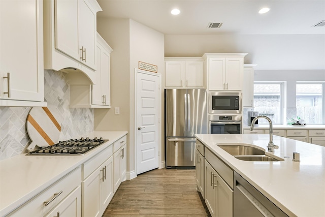 kitchen with sink, light hardwood / wood-style flooring, appliances with stainless steel finishes, tasteful backsplash, and white cabinetry