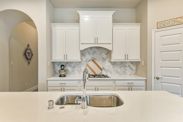 kitchen with backsplash, sink, white cabinets, and stainless steel gas stovetop