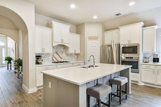 kitchen with decorative backsplash, stainless steel appliances, sink, white cabinets, and an island with sink