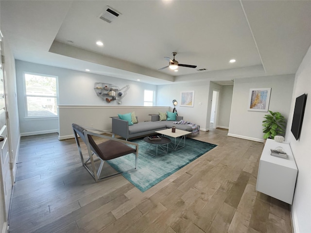 living room featuring a tray ceiling, ceiling fan, and light hardwood / wood-style floors