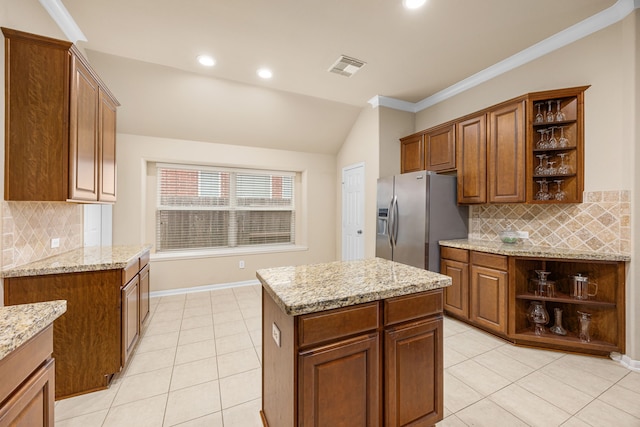 kitchen featuring light stone countertops, a center island, tasteful backsplash, stainless steel fridge with ice dispenser, and vaulted ceiling