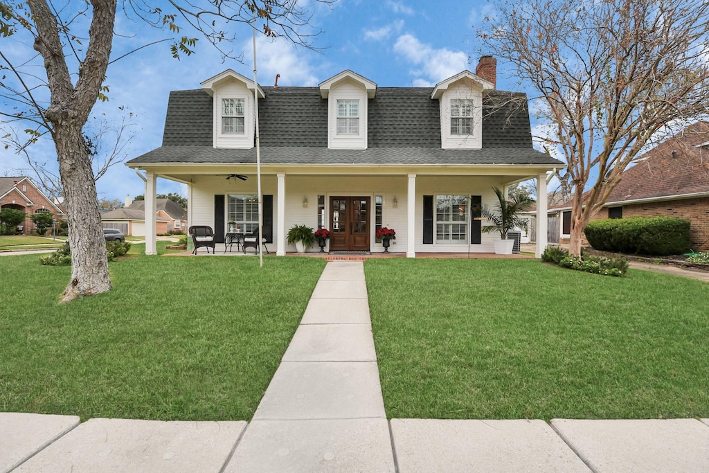 cape cod house with ceiling fan, covered porch, and a front lawn