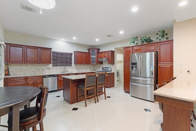 kitchen featuring appliances with stainless steel finishes, a breakfast bar, tasteful backsplash, washer / dryer, and sink