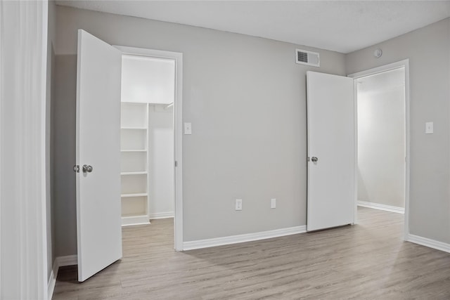 unfurnished bedroom featuring a walk in closet, a closet, and light wood-type flooring