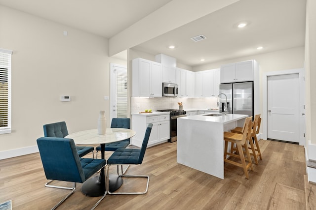 kitchen with a breakfast bar area, appliances with stainless steel finishes, a kitchen island with sink, light hardwood / wood-style floors, and white cabinets