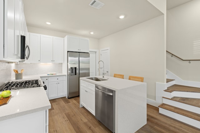 kitchen featuring sink, light hardwood / wood-style flooring, stainless steel appliances, white cabinets, and a center island with sink