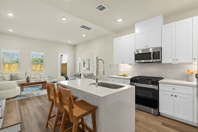 kitchen with sink, white cabinetry, light hardwood / wood-style flooring, an island with sink, and stainless steel appliances