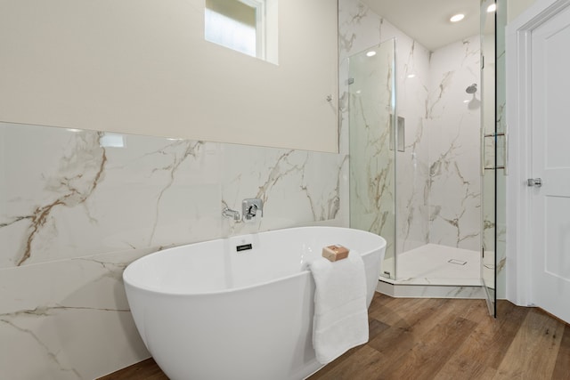 bathroom featuring plus walk in shower, hardwood / wood-style floors, and tile walls