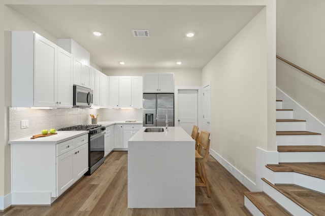 kitchen featuring sink, appliances with stainless steel finishes, white cabinetry, backsplash, and a center island with sink