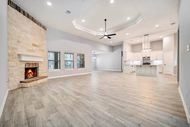 unfurnished living room with ceiling fan, a stone fireplace, light hardwood / wood-style flooring, and a tray ceiling