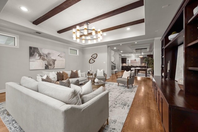 living room with a raised ceiling, hardwood / wood-style floors, a chandelier, and ornamental molding