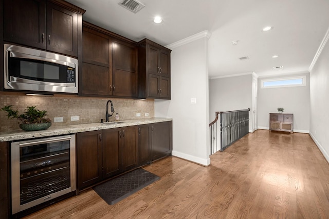 kitchen featuring stainless steel microwave, backsplash, sink, wine cooler, and light stone countertops