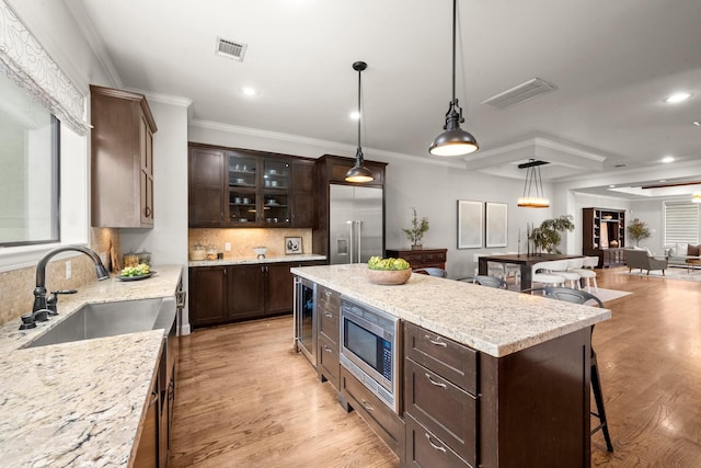 kitchen with dark brown cabinetry, a center island, sink, hanging light fixtures, and built in appliances